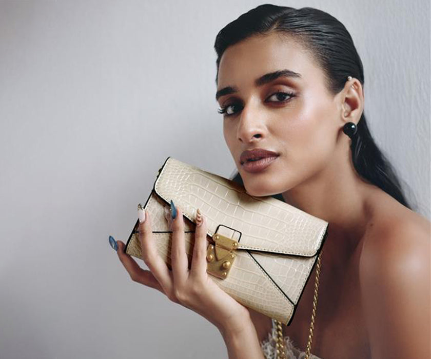 Woman holding a beige Miraggio shoulder clutch with gold chain detail.