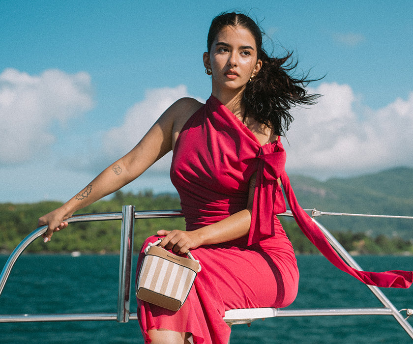 Woman sitting on a boat and holding a beige mini handbag.